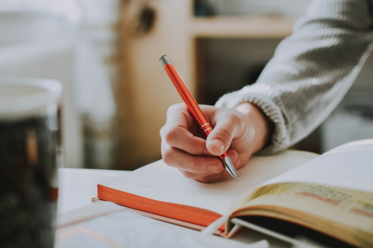 person holding on red pen while writing on book — Foto por lilartsy na Unsplash