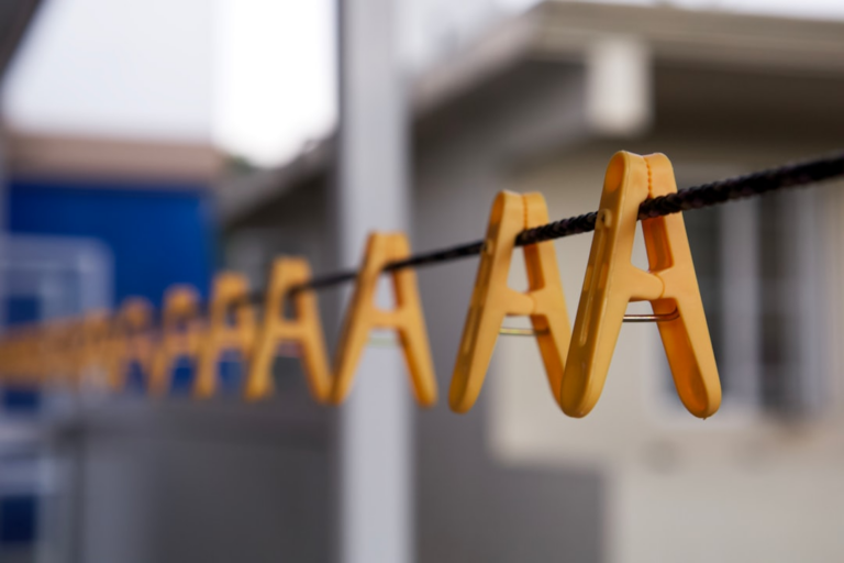 a wooden sign hanging on a rope in front of a building — Foto por Miguel Alcântara na Unsplash