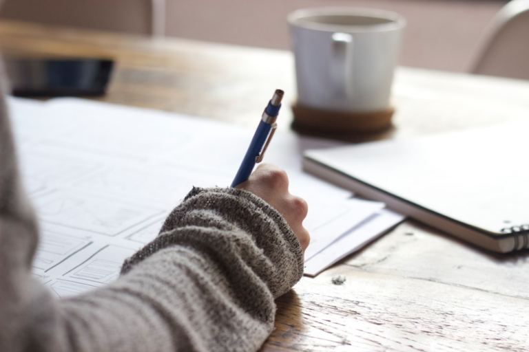 person writing on brown wooden table near white ceramic mug — Foto por Unseen Studio na Unsplash